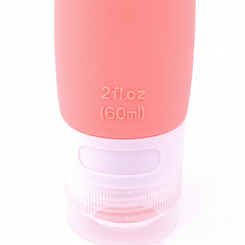 Close-up of 2 fl oz 60ml embossed measurement text and clear bottom cap on coral pink silicone travel bottle