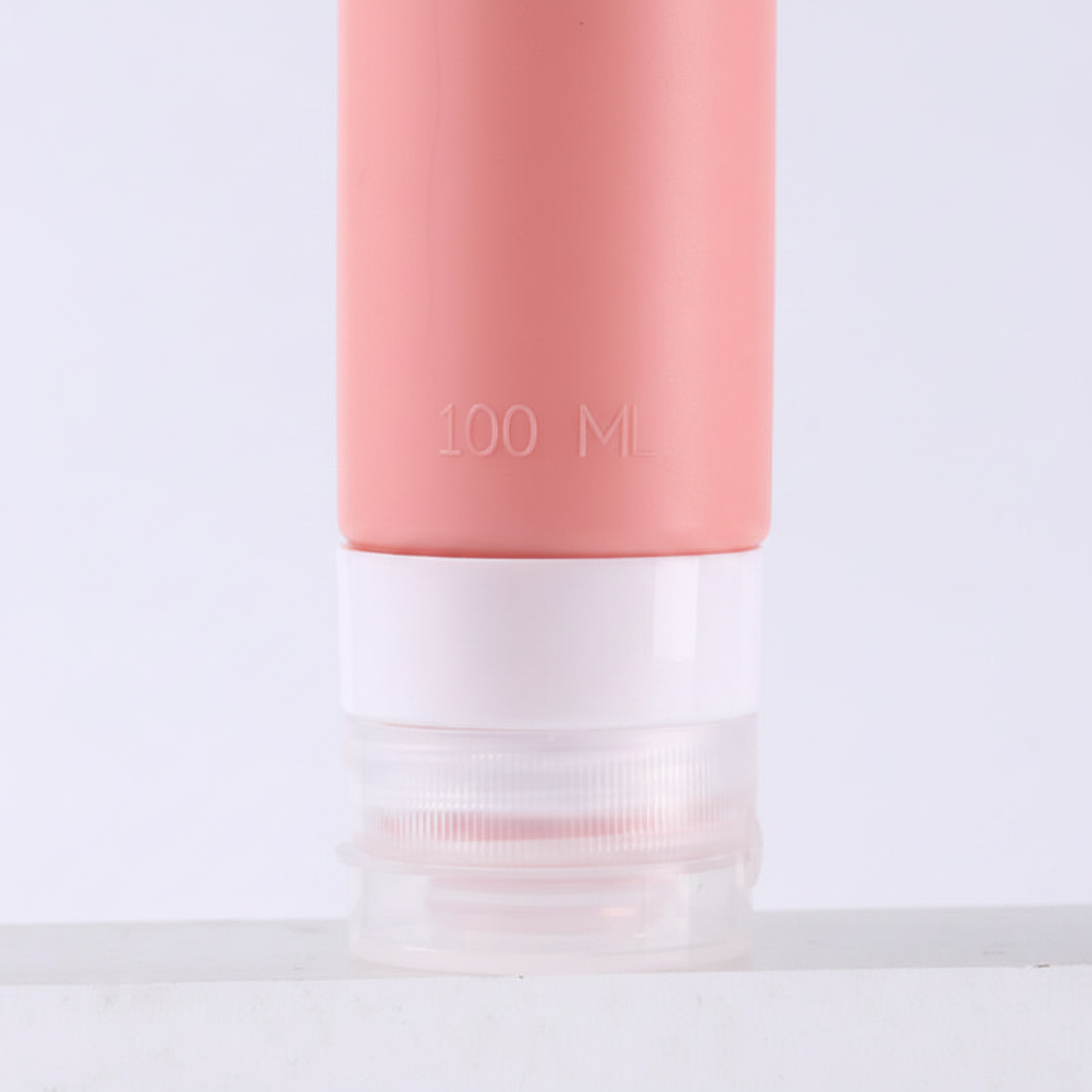 Close-up of clear bottom screw cap and 100ml embossed text on dusty rose pink silicone travel bottle on white background